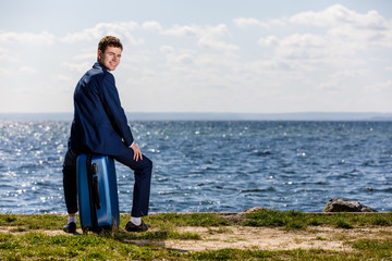 Businessman sitting on suitcase at seaside