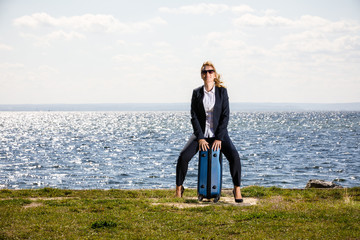 Businesswoman sitting on suitcase at seaside