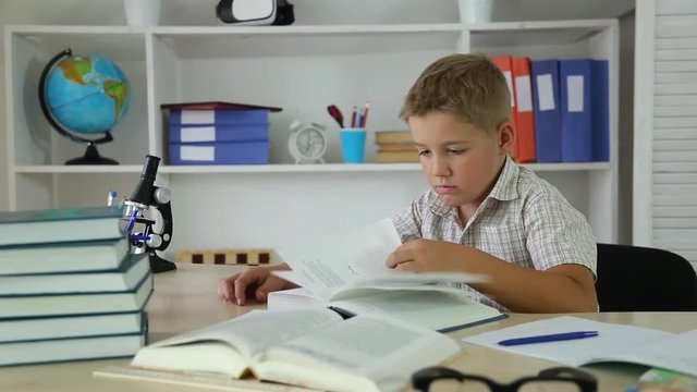 boy leafing through pages and reading a book sitting at Desk