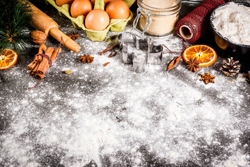 Christmas, New Year holiday cooking background. Ingredients, spices, dried oranges and baking molds, Christmas decorations (balls, fir-tree branch, cones), On black stone table, copy space