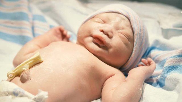 Newborn asian baby girl yawns as she rests gently in a crib in the hospital