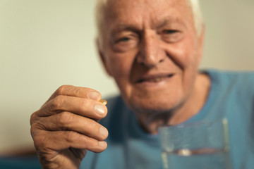 Fototapeta premium Senior Man Sitting On Bed At Home Taking Medication