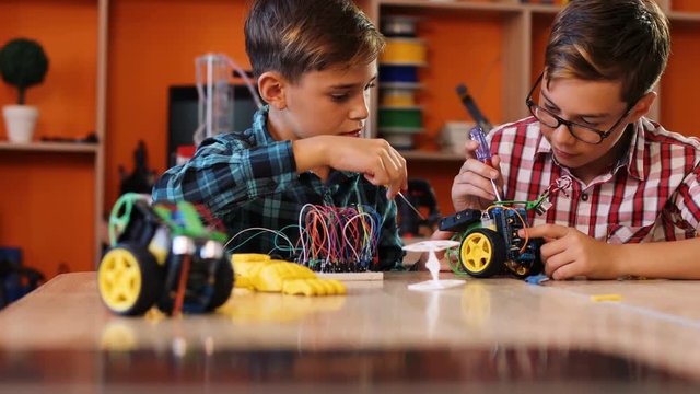 Close up of two boys assembling robots with screwdrivers on the table in the modern comfortable playing classroom. Portrait