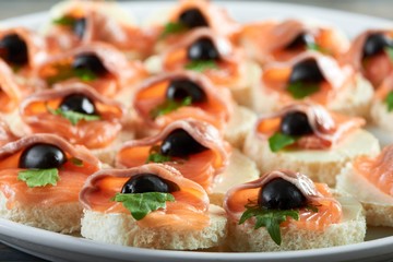 Cropped close up of small canapes with salmon and butter decorated with black olives food eating seafood fish appetizer tasty menu restaurant gourmet traditional fresh.