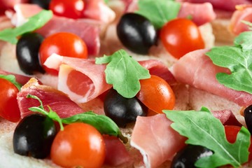 Cropped close op of ham black olives and cherry tomatoes served on canapes bread baked pastry buttered eating food restaurant vegetables rucola tasty delicacy gourmet menu.