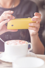 Woman photographed cup of coffee on a yellow smartphone. Toned