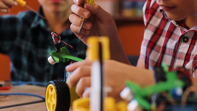 Close up of two happy boys using screwdrivers to put together robotic machines on the table in the modern playing space.