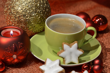 A coffee cup with star-shaped cinnamon biscuits, red and golden Christmas balls and a candle