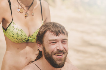 Woman in bikini makes hairstyle handsome man with a beard