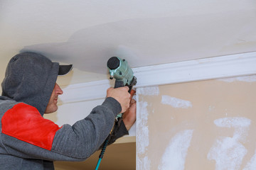 Carpenter brad using nail gun to Crown Moulding trim, warning label that all power tools