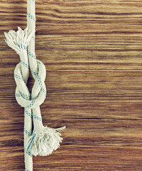 White rope and nautical reef knot on grunge wooden background with empty space.