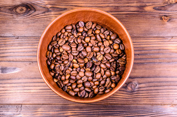Roasted coffee beans in bowl on wooden table. Top view