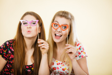 Two happy women holding fake eyeglasses on stick