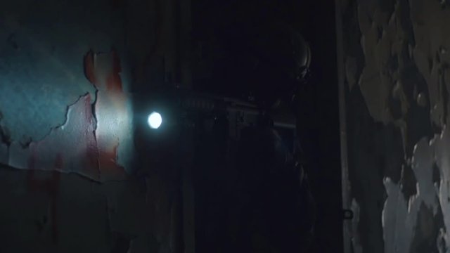Soldier in protective helmet looking in sight on gun with flashlight in dark