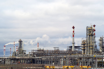general view of a chemical or oil refinery with a multitude of pipelines, factory pipes and distillation columns under a cloudy sky..