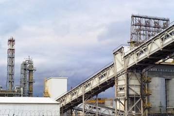 fragment of a modern industrial enterprise with silos for storage of loose materials, fractionating columns and an inclined covered belt conveyor