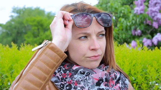 Dissatisfied girl looks at people. Woman on the park with sunglasses