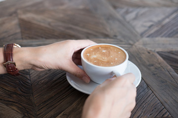 woman's hand holding hot cappuccino coffee in white cup in cafe