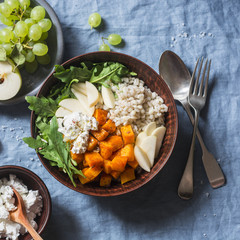 Baked butternut squash, barley, arugula and apples. Vegetarian buddha bowl with autumn vegetables and grains, on a blue background, top view
