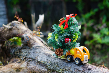 Miniature of lorry transportation toy with Christmas tree in blurred nature background. Holidays concept.