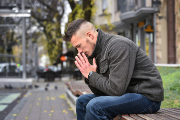 young sad man thinking while sitting on a bench in autumn