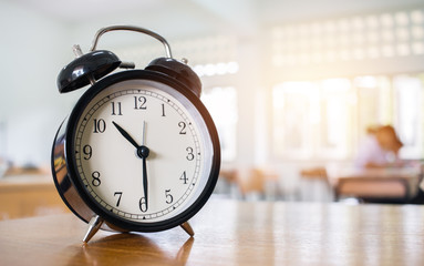 Closeup of Retro alarm clock with ten o'clock on table teacher in blur students exams classroom....