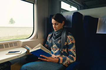 Pretty woman traveling by train sitting near window reading book