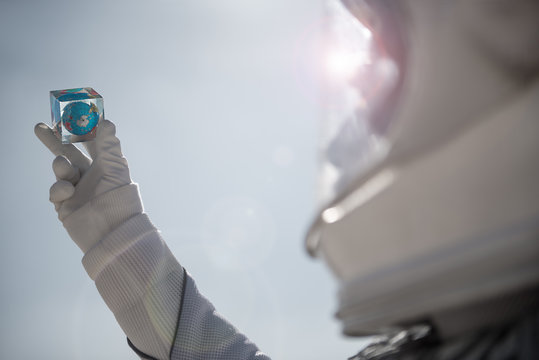 Astronaut is rising hands with small cube with globe. Close up of male arm. Copy space on right side. Low angle