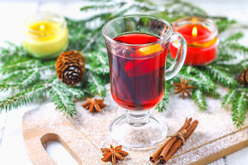Obraz na płótnie Canvas New Year's mulled wine in a glass on the background of twigs, candles and garlands.