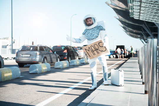 Trip to mars. Spaceman wearing strange armor is catching car. Full length portrait. Copy space on left side