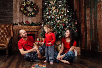 The family in pajamas plays next to a Christmas tree and a fireplace.