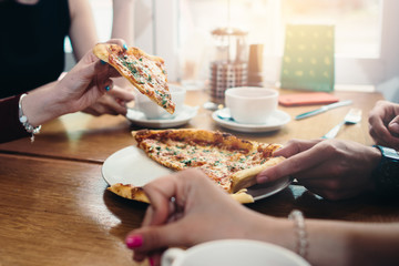 Close-up image of friends sharing traditional Italian pizza and drinking tea in a cafe