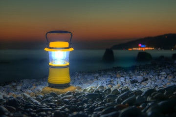 Luminous hand lantern standing on the pebble beach on the background of sea at dusk, Sochi, Russia
