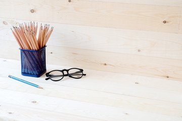 Graphite pencils in basket and eyeglasses isolated on wooden background