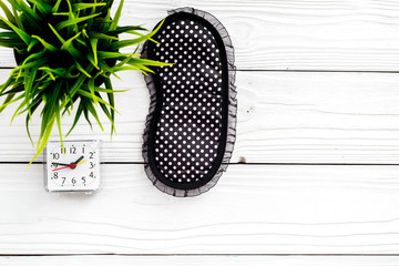 Fototapeta premium Healthy sleep concept. Sleep mask, plant, alarm clock on white wooden background top view copyspace
