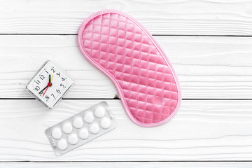 Combat insomnia. Sleeping pills near sleep mask and alarm clock on white wooden background top view