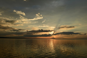 Fototapeta premium Sunlight from the clouds at sunset over the lake