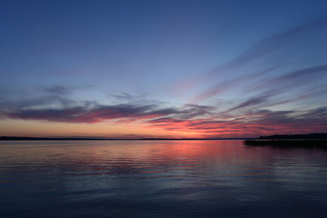 Sunlight at dusk in the sky above the quiet surface of the lake water