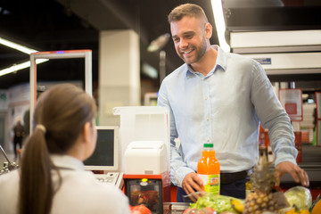 Portrait of handsome young man buying food in supermarket smiling happily at cashier scanning prices