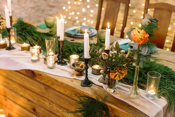 cosiness, celebration, silverware concept. lots of twinkle lights and burning candles illuminate decorated table of the restaurant with fresh branches of spruce and few orange roses