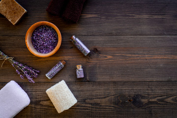 Fototapeta na wymiar Floral foot spa with lavender. Spa salt, sponge, soap, towel on dark wooden background top view copyspace