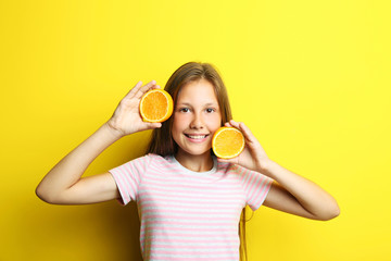 Portrait of beautiful girl with orange fruit on yellow background
