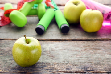 Green apple, skipping rope and dumbbells on wooden table
