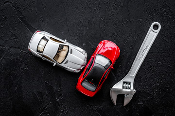 Car repair concept. Wrench near car toys on black background top view