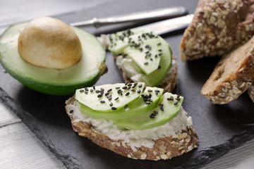 Healthy sandwiches with avocado, cottage cheese and whole wheat bread. Healthy breakfast served on black stone board ,white wooden table
