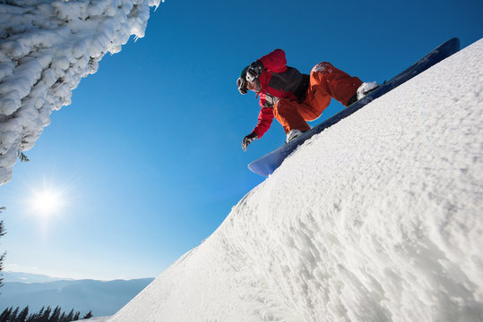 Low angle shot of a snowboarder preparing to riding downhill in the mountains on a beautiful sunny winter day. Blue sky, sun on the background freeride lifestyle active extreme adrenaline concept