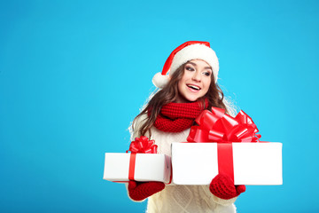 Beautiful young girl holding gift boxes on blue background