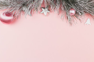 Christmas border with fir branches, christmas balls and silver ornaments on pastel pink background