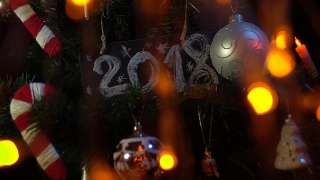 Plate numbered 2018 on a Christmas tree among toys and yellow electric lights, New Year's background.