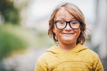 Close up portrait of adorable little kid boy wearing eyeglasses and yellow sweatshirt
